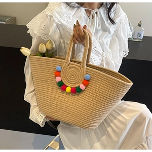Detail of straw woven tote bag featuring colorful pom-poms and bohemian holiday style