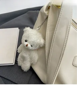 Close-up of white plush bear keychain accessory on cream leather bag with silver chain