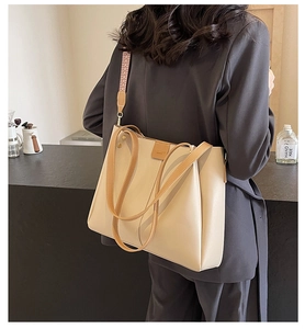 Detail of beige tote bag featuring brown leather handles and a woven geometric shoulder strap