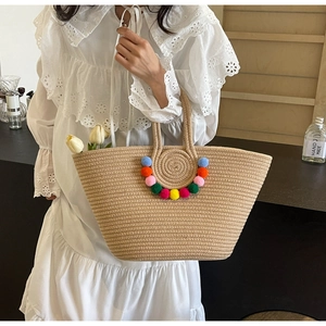 Detail of straw woven tote bag with colorful pom poms and handmade texture for summer