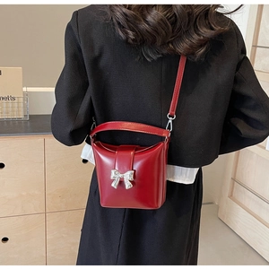 Détail d'un sac seau rouge brillant avec nœud argenté porté par un mannequin