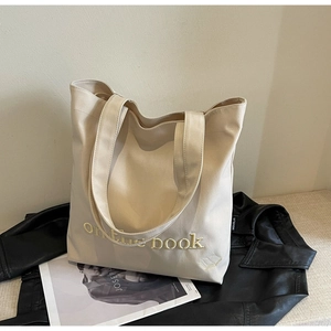 Detail of white canvas tote bag featuring on the book embroidery and golden book motif