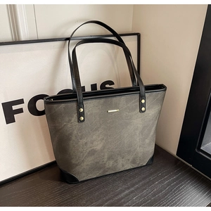 Detail of vintage grey leather tote bag with black handles and gold metal accents
