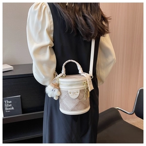 Détail d'un sac seau beige matelassé avec poignée tressée, foulard et charm peluche