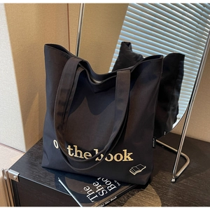 Detailed close-up of black canvas tote bag with yellow embroidery and woven label detail
