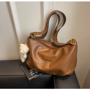 Detail of brown pleated tote bag featuring a leather label and a white teddy bear charm