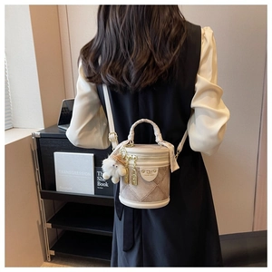 Détail du sac seau matelassé beige avec poignée tressée et breloque sur un mannequin