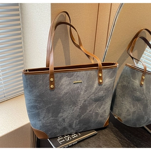 Detail of blue canvas tote bag featuring brown leather trim and golden rivets