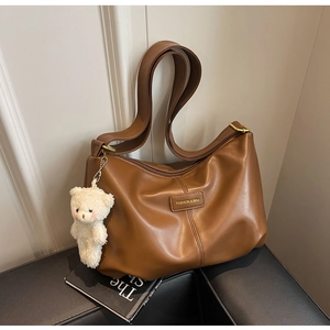 Detail of caramel tote bag with brand tag, wide strap and white plush bear charm