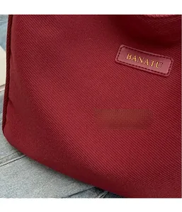 Close-up of wine red canvas tote bag with gold logo text on premium textured fabric