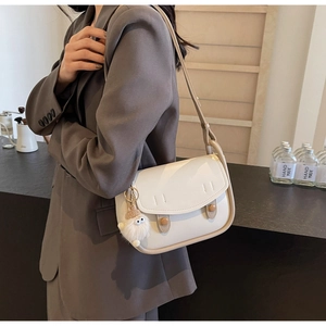 Detail of cream saddle bag featuring unique eye charm and smooth leather texture