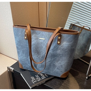 Detail of blue canvas tote bag featuring brown leather trim and gold metal logo plaque