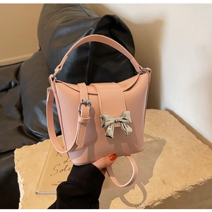 Détail du sac en cuir rose clair avec un nœud métallique argenté sur socle en pierre