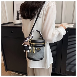Détail du sac seau en denim gris avec breloque peluche et foulard à damier sur l'anse