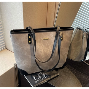 Close-up of a large grey tote bag with black trim and a gold logo in a chic interior setting