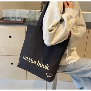 Detail of black canvas tote bag with on the book embroidery and MIDUOLAI side label