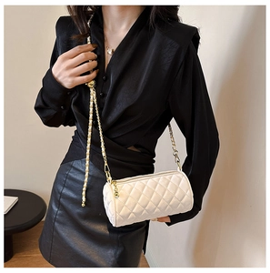 Macro detail of white quilted cylinder bag with gold chain strap on a model