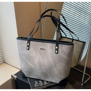 Detail of dark grey tote bag featuring gold logo plate and reinforced black corners