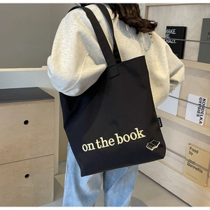 Rear view of black canvas tote bag on shoulder showing large capacity and book print