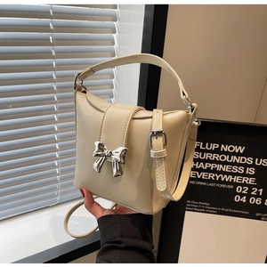 Détail du sac seau crème avec un grand nœud en métal argenté et une texture en cuir lisse