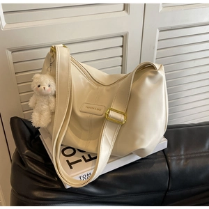 Detail of off-white pleated hobo bag with adjustable strap and plush bear charm decoration