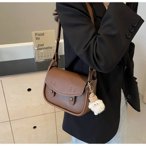 Detail of a brown leather saddle bag with vintage buckles and a plush charm