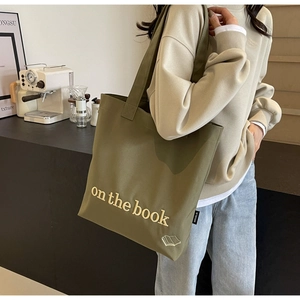 Detail of olive green canvas tote bag featuring white book embroidery and woven side label