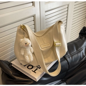 Detailed shot of cream pleated hobo tote bag with plush bear charm on a fashion book