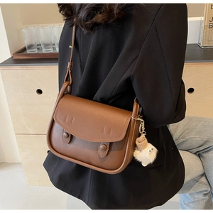 Close-up of brown leather saddle bag with decorative buttons and white plush charm detail