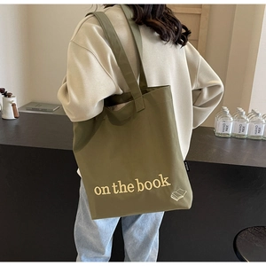 Olive green canvas tote bag with yellow print shown being worn by a person