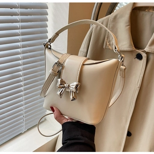 Détail d'un sac seau beige avec boucle noeud en métal argenté et texture cuir brillant