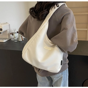 Detail of white corduroy hobo bag with Banatu leather label in a warm cafe setting