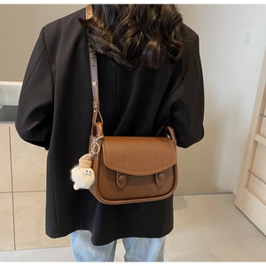 Detail of a dark brown vintage saddle bag featuring a cute white plush charm on the strap
