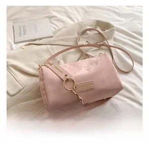 Detail of pink matte cylindrical Boston bag with gold hardware on a cozy white bedsheet