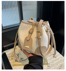 Detail of hand-woven bucket bag with beige leather strap and gold metal hardware