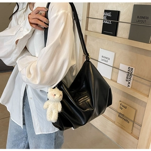 Detail of black pleated tote bag featuring a cute white plush bear charm on the strap