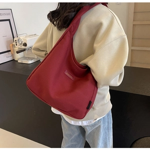 Detail of burgundy canvas tote bag with BANAIU logo plaque and wide shoulder strap
