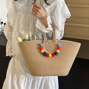 Large straw tote bag with colorful pom-poms for beach vacation and summer styling