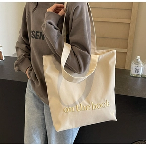 Detail of beige canvas tote bag featuring embroidered 'on the book' text and wide strap