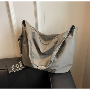 Sac bandoulière minimaliste en nylon gris avec large sangle sur un canapé en cuir noir