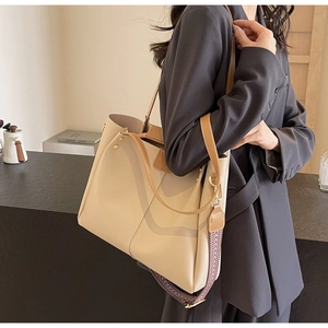 Beige tote bag detail showing wide geometric shoulder strap and leather texture