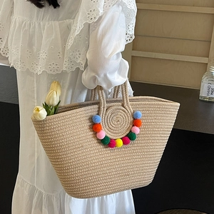 Handwoven beige straw tote bag with colorful pom-pom decor and circular handles