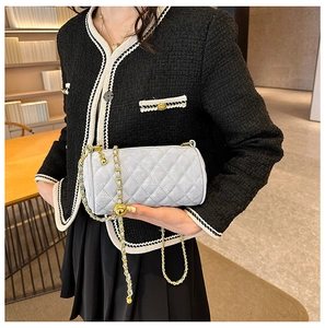 Detail of light blue quilted cylinder bag with gold chain strap and decorative ball