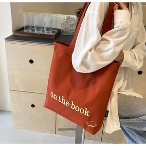 Detail of rust red canvas tote bag with book embroidery and side brand woven label