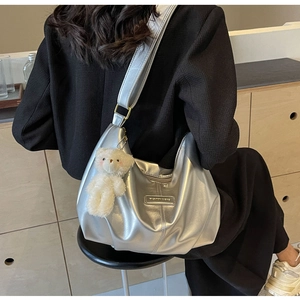 Silver crescent hobo bag with teddy bear charm and metal logo on model's shoulder