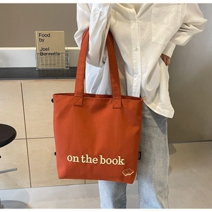 Detail of red canvas tote bag featuring white embossed 'on the book' text and wide handle