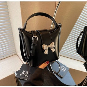 Détail d'un sac à main noir minimaliste avec nœud argenté sur fond texturé