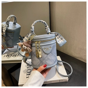 Détail du sac seau en denim bleu clair avec coutures matelassées et breloque peluche