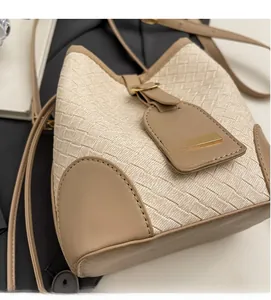 Close-up of woven bucket bag featuring cream fabric and light brown leather trim detailing