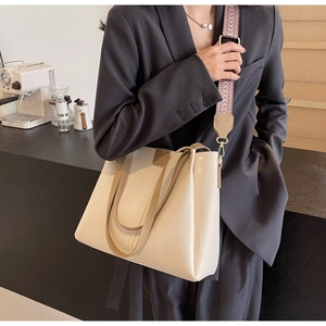 Detail of cream tote bag with brown leather handles and textured wide shoulder strap